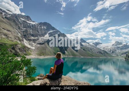 Mädchen sitzen und genießen schöne Aussicht auf Bergsee in der Nähe Kaprun,Österreich.ruhige Entspannung im Freien.wunderbare Naturlandschaft,türkisfarbenes Wasser,Urlaub Stockfoto