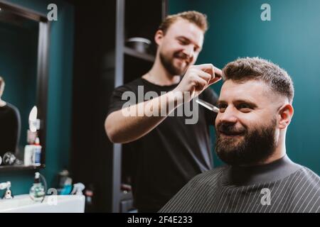 Barbier junger Mann macht Frisur zu glücklich bärtigen männlichen Kunden in Friseurladen. Stockfoto