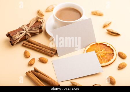 Komposition aus grauen Papier Visitenkarten, Mandeln, Zimt und Tasse Kaffee. Mockup auf orangefarbenem Hintergrund. Leer, Seitenansicht, Standzeit, Kopierbereich. Stockfoto