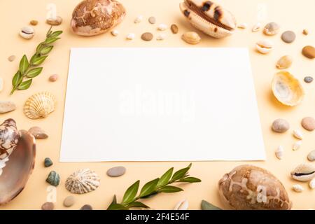 Komposition mit weißem Papierblatt, Muscheln, Kieselsteinen, grünem Buchsbaum. Mockup auf orangefarbenem Hintergrund. Leer, Seitenansicht, Stillleben, Kopierraum. Reise c Stockfoto