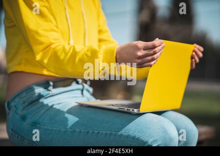 Eine Nahaufnahme der Hände eines Mädchens, die ihr Gelb justieren Laptop-Bildschirm balanciert auf den Knien im Park Stockfoto