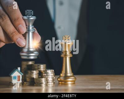Hand des Geschäftsmannes hält goldenen König Schach und zu Hause auf Münzen Stapel erfolgreich mit Streulicht. Gewinner des Geschäfts und erfolgreich, Manageme Stockfoto