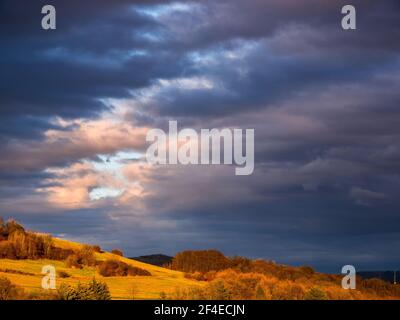 Ein Riss in dichten Wolken am Himmel über einem Hügel am Abend von der Sonne beleuchtet Stockfoto