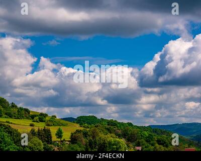 Massive Wolken - Cumulus congestus oder hoch aufragender Cumulus - bilden sich Im blauen Himmel über hügeliger Landschaft Stockfoto