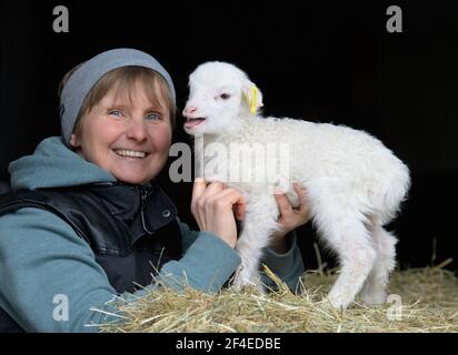 Roskow, Deutschland. März 2021, 15th. Bäuerin Katja Behling vom Skuddenhof im Weseram-Kreis Roskow streichelt das am 7. März 2021 geborene Lamm Danika. Zusammen mit ihrem Mann betreibt die gelernte Einzelhandelskauffrau die Zucht von Skudden, der kleinsten einheimischen Schafrasse, die zu den ältesten Hausschafrassen zählt und weiße Mischwolle produziert. Die Skudde steht auf der Roten Liste der vom Aussterben bedrohten Nutztierrassen. (Zu 'Lambing Time: Nachzucht ist ein wirtschaftlicher Faktor für Schafzüchter') Quelle: Soeren Sache/dpa-Zentralbild/ZB/dpa/Alamy Live News Stockfoto