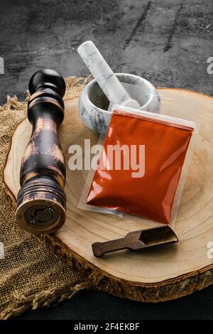 Holzquerschnitt mit geräuchertem Paprika in Kunststoffverpackung und Steinmörtel und Mühle Stockfoto