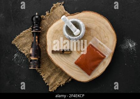 Holzquerschnitt mit Chilischote in Plastikverpackung und Steinmörtel und Mühle Stockfoto