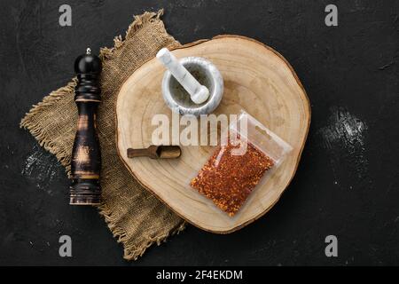 Holzquerschnitt mit Chilischoten in Kunststoffverpackung und Steinmörtel und Mühle Stockfoto