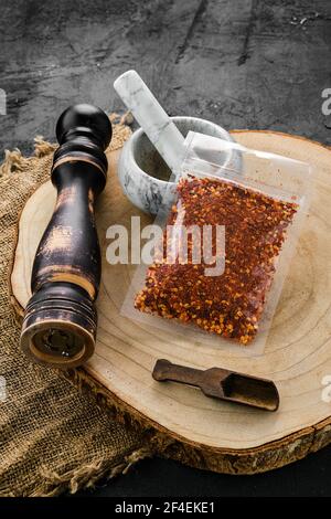 Holzquerschnitt mit Chilischoten in Kunststoffverpackung und Steinmörtel und Mühle Stockfoto