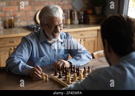 Lächelnder älterer Vater spielt Schach mit erwachsener Sohn Stockfoto