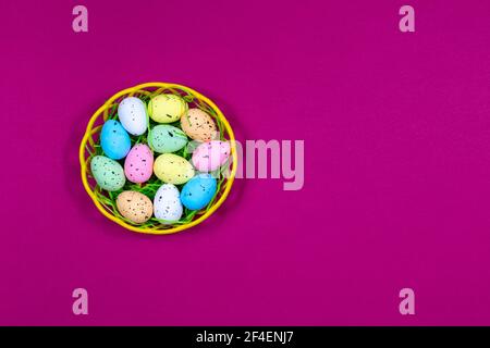 Bunte Ostereier in einer Schüssel auf einem Himbeerrot Hintergrund. Platz für eine Inschrift. Blick von oben. Ostern. Stockfoto