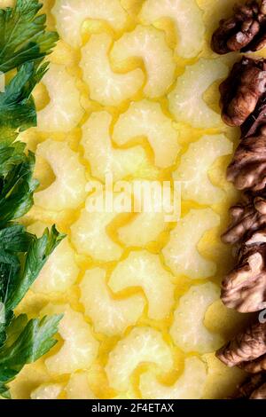 In Scheiben geschnittener halbmondförmiger Sellerie, umrandet mit Walnuss und Petersilie auf einem Nahaufnahme mit gelbem Hintergrund Stockfoto