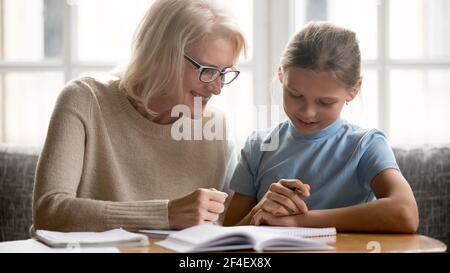Lächelnde Großmutter und Enkelin machen gemeinsam Hausaufgaben Stockfoto