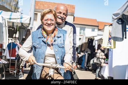 Glückliches Seniorenpaar mit Spaß auf dem Fahrrad auf dem Stadtmarkt - aktiv spielerisch ältere Konzept Fahrrad zum Ruhestand Zeit - Alltagslebensfreude Stockfoto