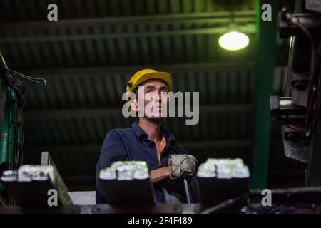 Aluminiumelektrolyseanlage. Gießereilinie für Barren. Erwachsene asiatische Arbeiter Operator in gelben Arbeitshelm. Stockfoto