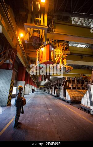 Aluminium-Elektrolyse-Anlage.Bedienpersonal mit Fernbedienung in gelbem Hardhat und Atemschutzmaske (links). Schlackenhandling Kran, Elektrolyse Bäder Zellen Stockfoto