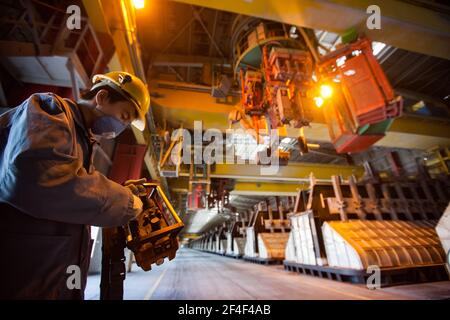 Aluminiumelektrolyseanlage. Bedienpersonal mit Fernbedienung in gelber Schutzhaube und blauem Atemschutzgerät. Schlackenhandling Kran und Elektrolysebäder auf Stockfoto