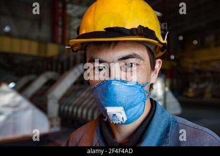 Aluminiumelektrolyseanlage. Junge asiatische Arbeiter Porträt. Kranführer für die Schlackenhandhabung. In gelbem Hardhut und blauem Atemschutzgerät. Elektrolysebäder auf b Stockfoto