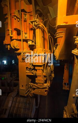 Aluminiumelektrolyseanlage. Nahaufnahme der Maschine für die Handhabung von Schlacken. Mechanische Elemente (Teile) in orangefarbenem Licht. Stockfoto
