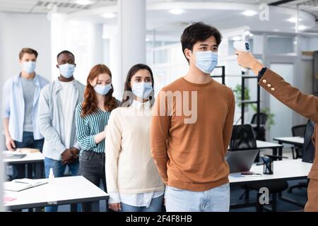 Person mit kontaktlosem Thermometer Cheking verschiedene Menschen Temperatur in der Warteschlange Stockfoto