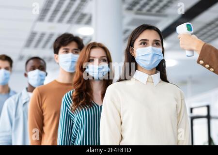 Frau mit kontaktlosem Thermometer Cheking multirassischen Menschen Temperatur in der Schlange Stockfoto