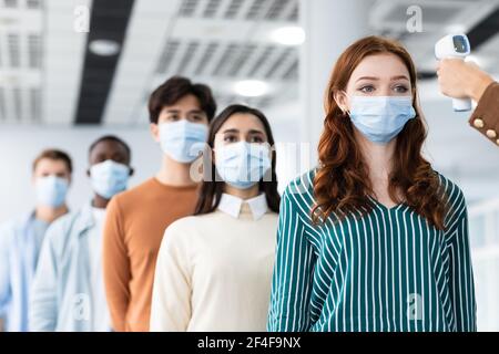 Frau mit kontaktlosem Thermometer Cheking verschiedenen Menschen Temperatur in der Schlange Stockfoto