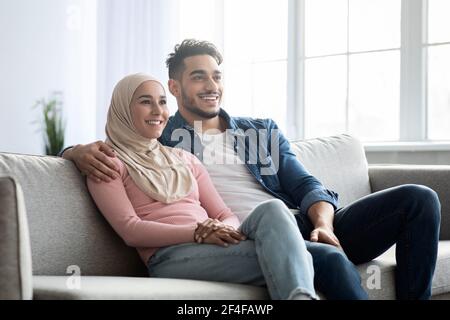 Fröhliche muslimische Familie sitzt auf dem Sofa zu Hause Stockfoto