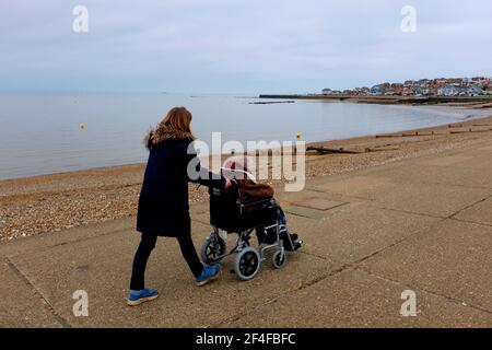 Frau, die einen Rollstuhl mit einer behinderten Frau sitzt in schieben hampton-on-Sea East kent uk märz 2021 Stockfoto