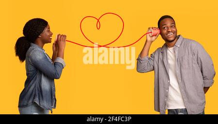 Love Message. Schwarze Frau flüstert romantische Worte an Freund über Zinn-Telefon Stockfoto