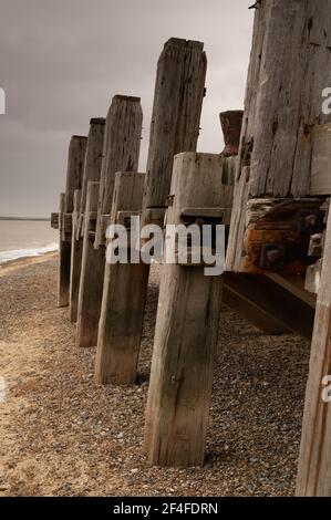 Eine Reihe verfallender Holzsäulen am Ende von Ein Norfolk Pier steht im Sand Stockfoto