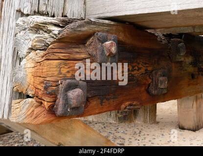 Verfallende Holzbalken am Ende eines Piers in norfolk england, wo die Salzseeluft und das Wasser alle großen Muttern und Bolzen erodiert und verrostet haben. Stockfoto