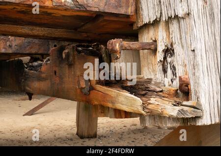 Verfallende Holzbalken am Ende eines Piers in norfolk england, wo die Salzseeluft und das Wasser alle großen Muttern und Bolzen erodiert und verrostet haben. Stockfoto