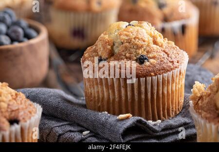 Nahaufnahme eines Blaubeer Muffins auf einer Stoffserviette mit Muffins auf einem Kühlregal im Hintergrund Stockfoto