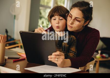 Mutter und Sohn sitzen zu Hause mit einem digitalen Tablet am Tisch. Mutter lehrt, wie man auf digitalen Tablet zu Sohn schreiben. Stockfoto