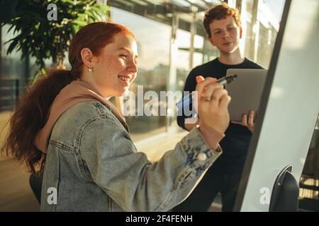 Schüler schreiben auf Whiteboard im Klassenzimmer. Studentinnen schreiben an Bord während des Gruppenstudiums in der Klasse. Stockfoto