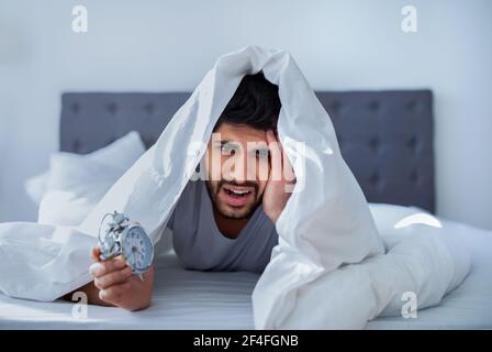 Arabischer Mann, der unter Schmerzen leidet, im Bett unter der Decke liegt und morgens aufwacht Stockfoto