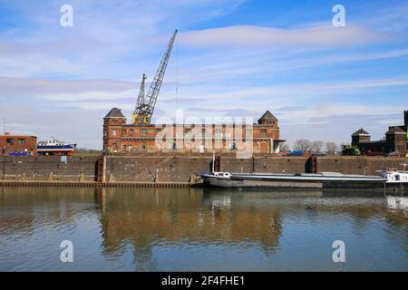 Krefeld (Ürdingen) - März 1. 2021: Blick auf alten Binnenladerhafen am Rhein mit Kran, Wasserschiff und Fabrikgebäude gegen Blue sk Stockfoto