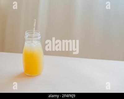 Glasflasche mit gelbem Saft vereist und Papierstroh auf Holztisch. Sommerfrucht Drink Minimales Konzept. Vorderansicht. Stockfoto