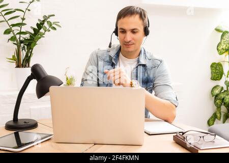 Fokussierter junger Geschäftsmann in Brillen mit Kopfhörern, hält Videoanruf mit Kunden auf Laptop. Konzentrierter tausendjähriger Mann in Gläsern geben Stockfoto