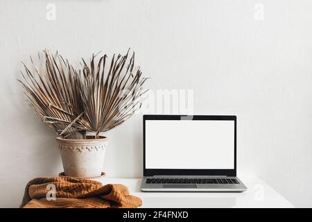 Tropischer Sommer Home Office Stillleben Zusammensetzung. Schwarzer Laptop-Mockup mit leerem Computerbildschirm. Trockene Palmblätter im Blumentopf. Weiße Wand Stockfoto