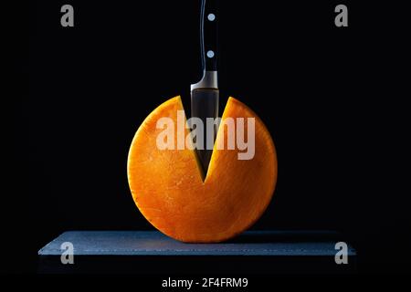 Große Runde Hartkäse mit Messer auf dem Schiefertisch im dunklen Hintergrund. Stockfoto