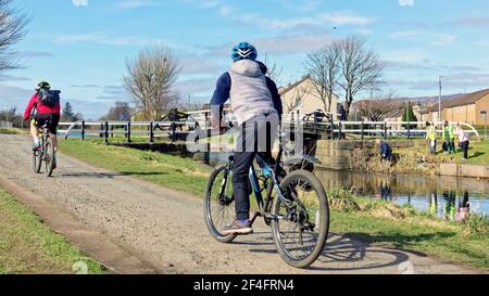 Glasgow, Schottland, Großbritannien. März 2021, 21st. Wetter in Großbritannien: An einem sonnigen Tag kehrte der Frühling in die Stadt zurück, als viele Menschen auf dem Schleppweg des Forth und clyde Kanals spazierten und Rad fuhren und vorcovid Szenen sahen. Als Freiwillige Kanalarbeiter säubern den Müll und entfernen die Oblekte aus den Wasserstraßen im Hintergrund. Quelle: Gerard Ferry/Alamy Live News Stockfoto