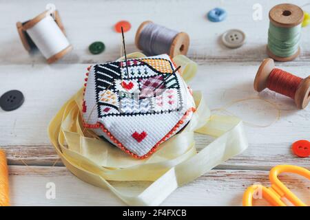 Handgefertigtes Nadelkissen mit schlichtem Ornament und Nadeln auf dem weißen Schreibtisch. Accessoires auf den Hintergrund nähen. Stockfoto