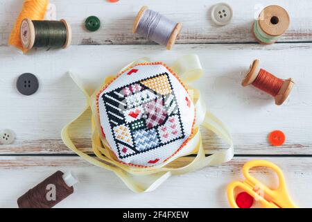 Handgefertigtes Nadelkissen mit schlichtem Ornament auf dem weißen Schreibtisch. Blick von oben. Stockfoto