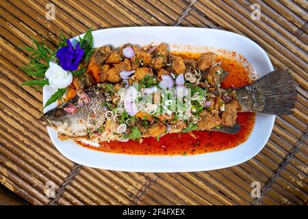 Thailändische Gerichte aus gebratenem Schnapper mit gemischtem Salat aus frischen Kräutern und Gewürzen wie Chili, Knoblauch, Zwiebel in kleine Stücke gemacht gekrönt. Mit Würze Stockfoto