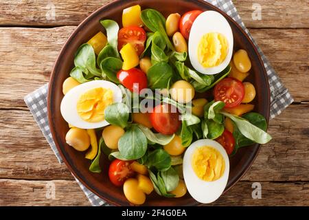 Vitaminleckerer Salat aus Lupinen, gekochten Eiern, Tomaten und gemeinem Cornsalat in Nahaufnahme auf einem Teller auf dem Tisch. Horizontale Draufsicht von oben Stockfoto