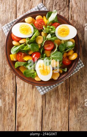 Diätsalat aus Lupinen, gekochten Eiern, Tomaten und Nusssalat in Nahaufnahme auf einem Teller auf dem Tisch. Vertikale Ansicht von oben Stockfoto