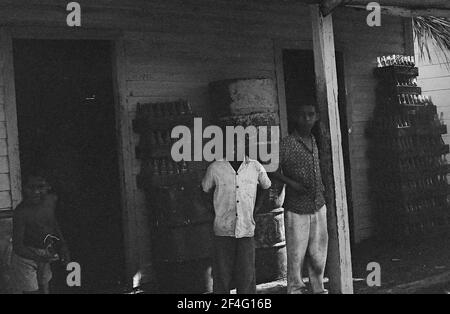 Die Menschen versammeln sich unter einem Strohdach mit Coca Cola Flaschen sichtbar, in der Sierra Maestra Berge, Kuba, 1963. Aus der Sammlung Deena Stryker Photographs. () Stockfoto