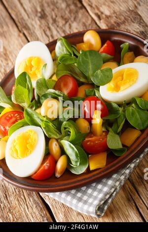 Frischer Salat aus Lupinen, Eiern, Tomaten und Valerianella locusta in Nahaufnahme auf einem Teller auf dem Tisch. Vertikal Stockfoto