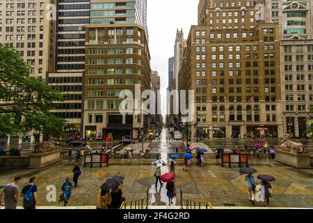 Die Straßenansicht der 5th Avenue von New York Public Library Main Branch an einem regnerischen Tag mit Menschen, die mit ihren Sonnenschirmen spazieren Stockfoto